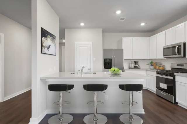 a kitchen with stainless steel appliances granite countertop a sink a stove a refrigerator with white cabinets and wooden floor