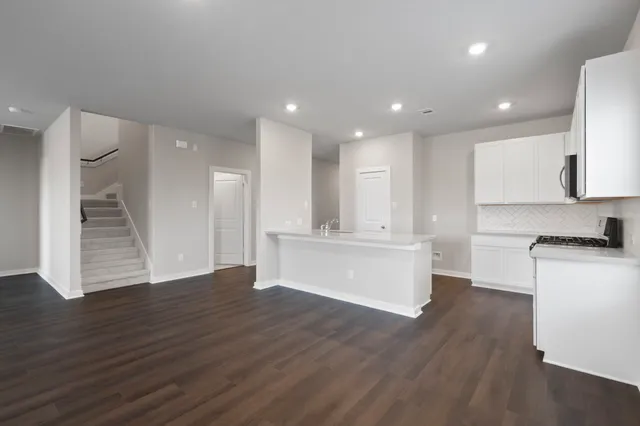 a view of an empty room and kitchen with wooden floor