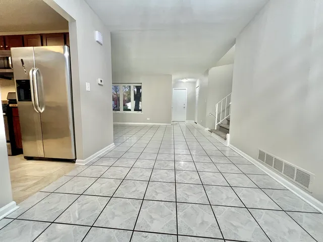 a view of a refrigerator in kitchen and an empty room in wooden floor