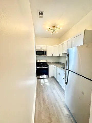 a kitchen with stainless steel appliances granite countertop a refrigerator a stove a sink and white cabinets