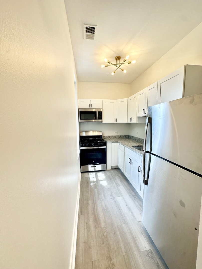 3008 West 23rd Street, Unit 2B Chicago, IL 60623 - Photo 9 of 10 a kitchen with stainless steel appliances granite countertop a refrigerator a stove a sink and white cabinets
