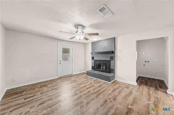 a view of an empty room with wooden floor fireplace and a window