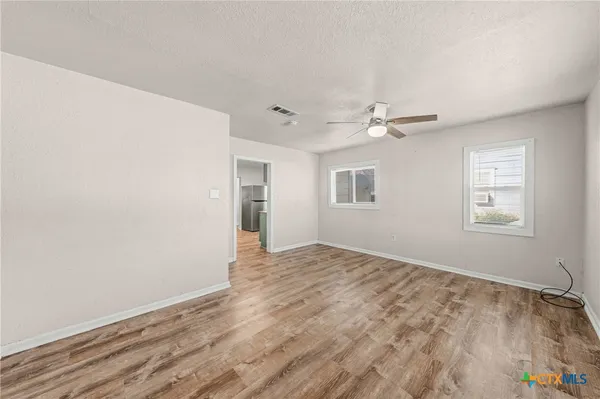 a view of empty room with wooden floor and fan