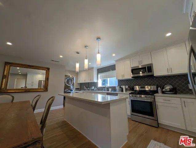 a kitchen with stainless steel appliances granite countertop a stove a sink a microwave a refrigerator white cabinets and wooden floor