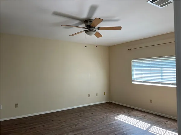 an empty room with wooden floor fan and windows