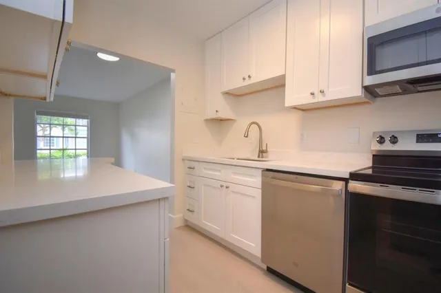 a kitchen with stainless steel appliances granite countertop a sink dishwasher a stove and white cabinets with wooden floor