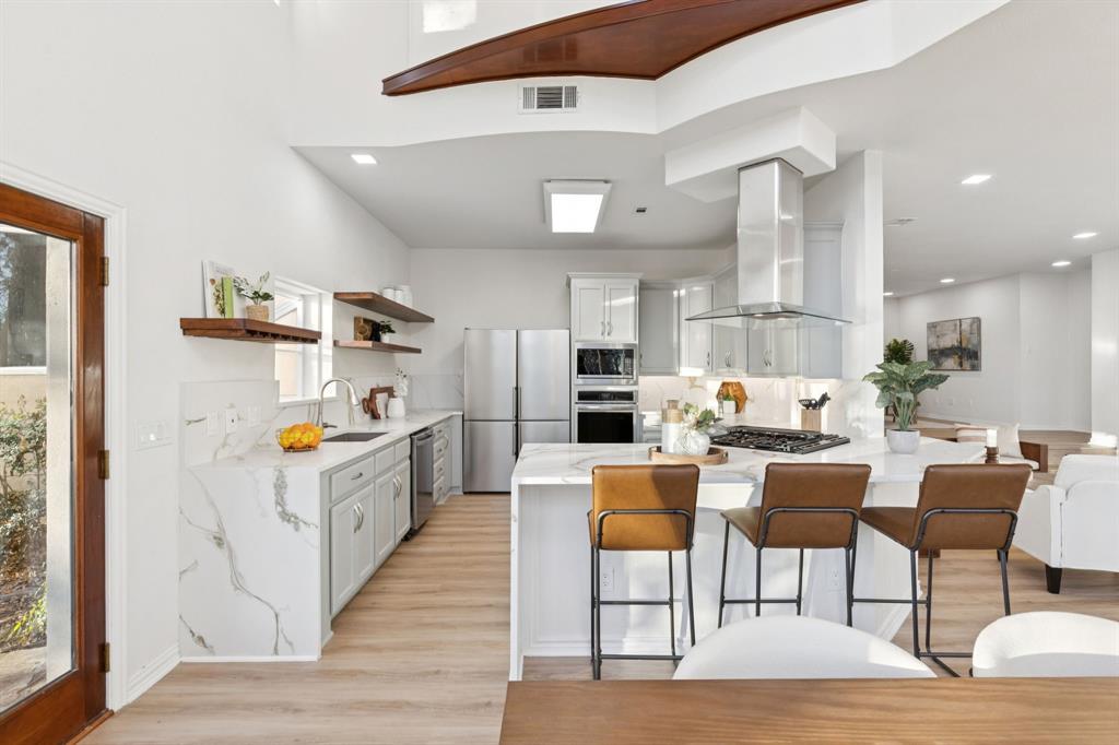 540 Diamond Point Drive Oak Point, TX 75068 - Photo 8 of 27 Kitchen with light stone countertops, a peninsula, appliances with stainless steel finishes, ventilation hood, and white cabinetry