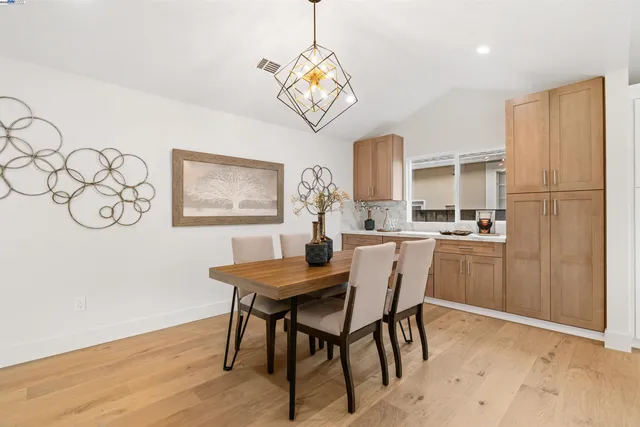a kitchen with a dining table chairs wooden floor cabinets and appliances