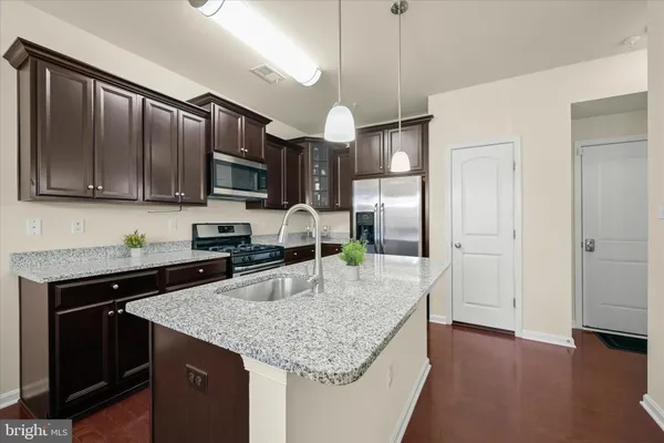a kitchen with granite countertop stainless steel appliances a sink dishwasher a refrigerator a stove top oven a large island with wooden floor and cabinets