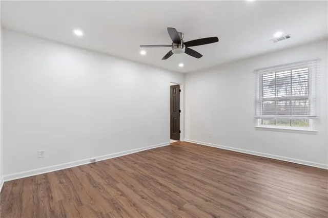an empty room with wooden floor fan and windows