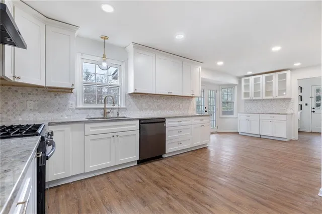 a kitchen with stainless steel appliances granite countertop a stove a sink and white cabinets with wooden floor