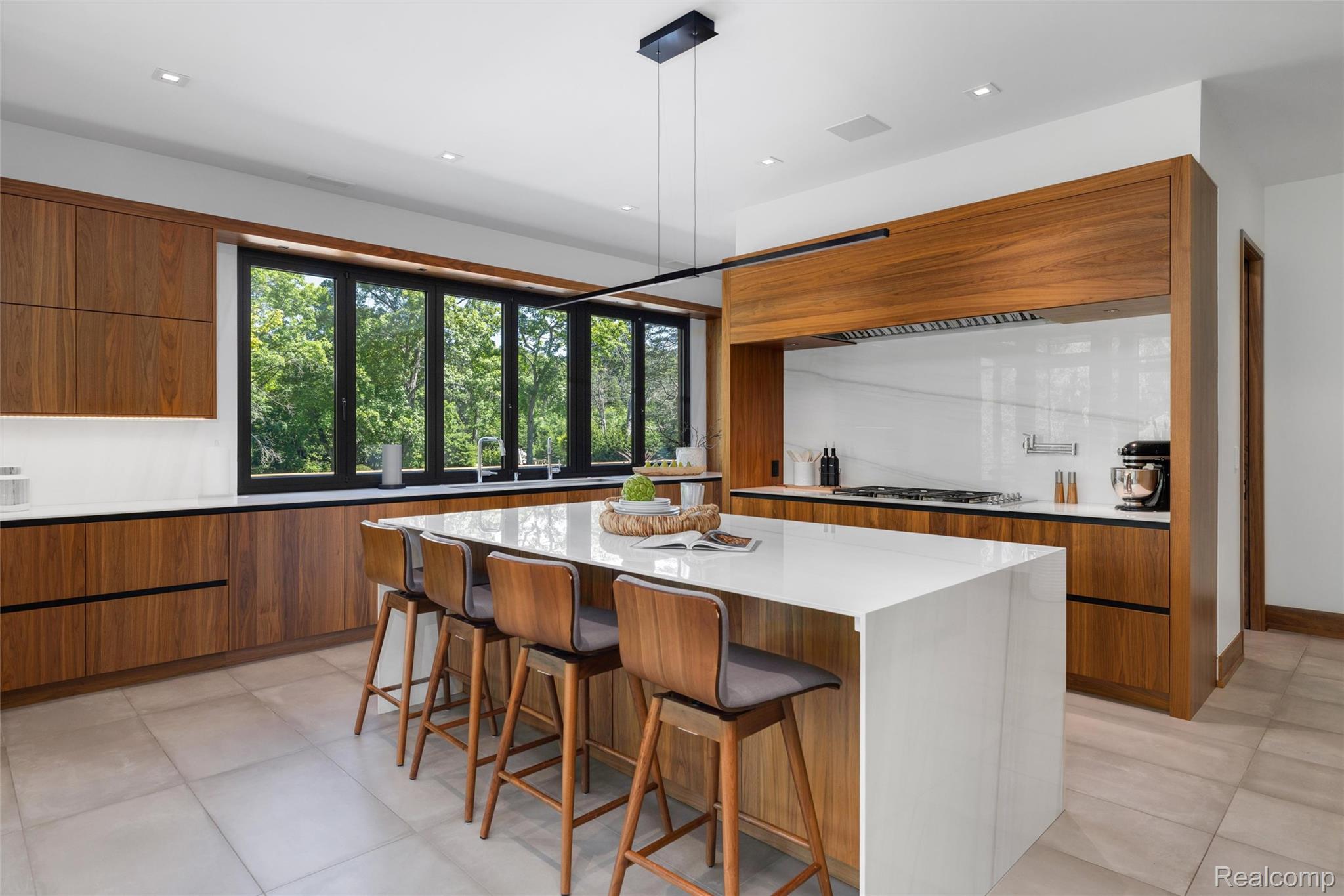 2700 Squirrel Road Bloomfield Hills, MI 48304 - Photo 16 of 83 Modern kitchen featuring a large waterfall-edge island with seating, extensive wood-finish cabinetry, a sleek linear pendant light fixture, a built-in range with a contemporary hood, and a white countertop with a matching backsplash