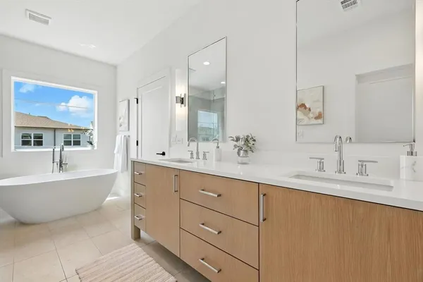 a spacious bathroom with double vanity a mirror a bathtub and window