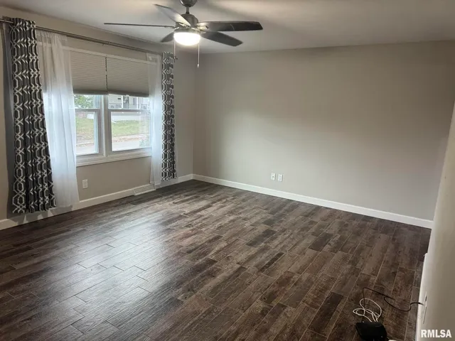 an empty room with wooden floor fan and windows