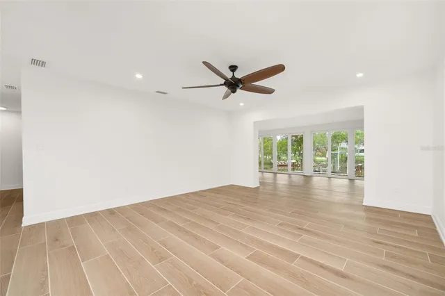 an empty room with wooden floor fan and windows
