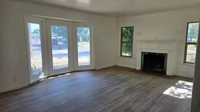 an empty room with wooden floor fireplace and windows