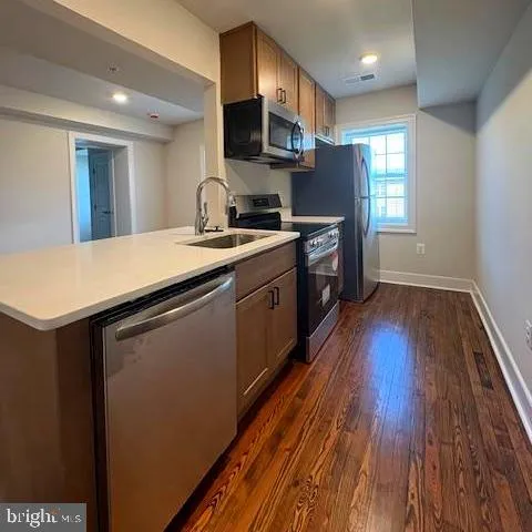 a kitchen with stainless steel appliances granite countertop wooden cabinets a sink a stove a refrigerator and island