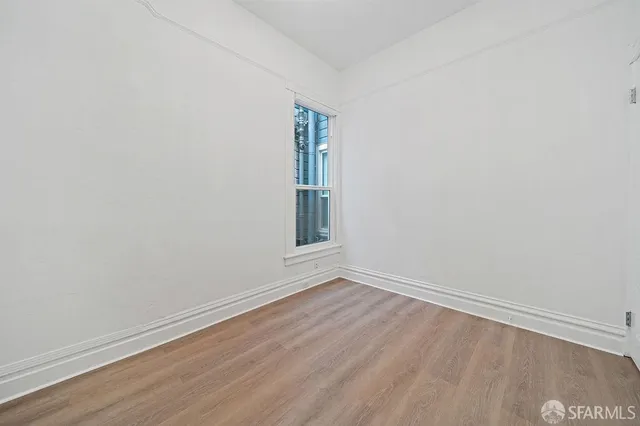 a view of an empty room with wooden floor and window