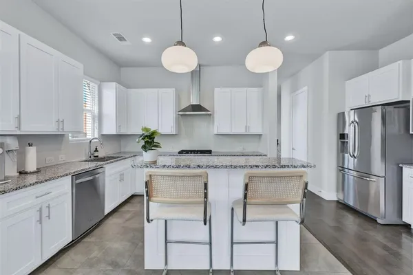 a kitchen with stainless steel appliances granite countertop a sink a stove a refrigerator and island with wooden floor