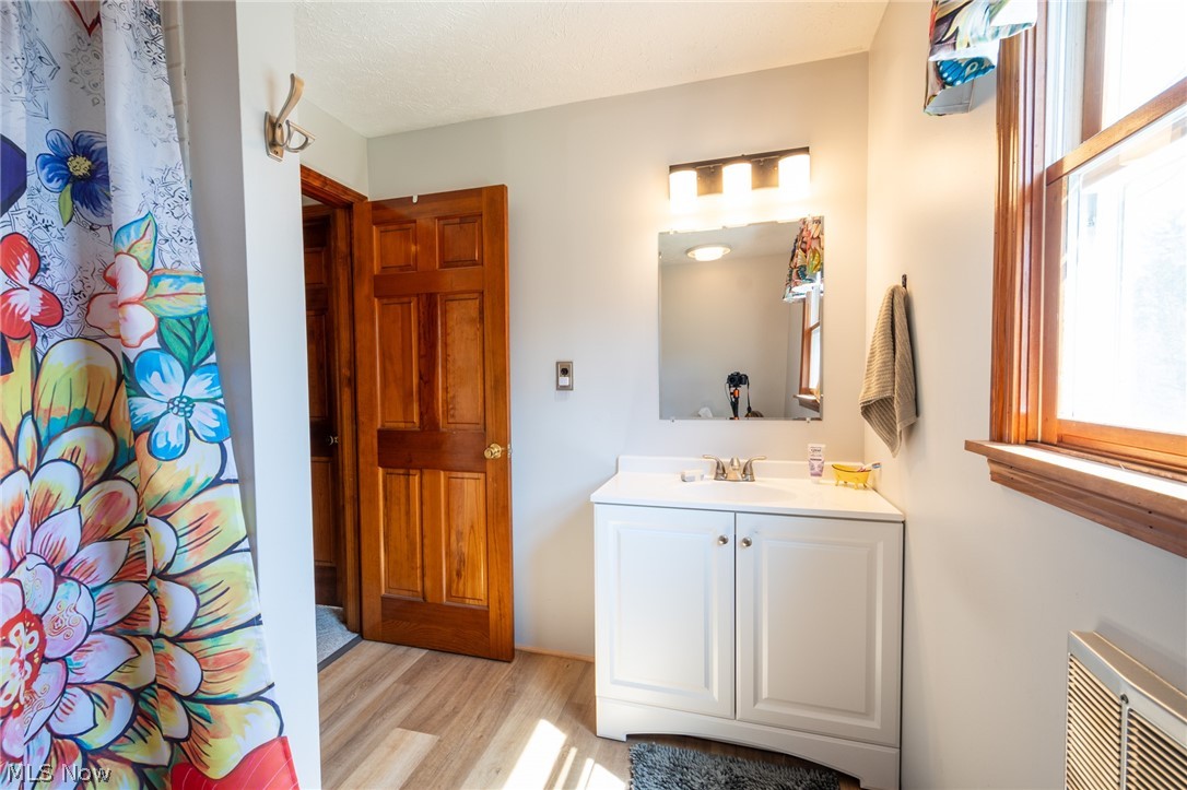 14027 Mayfield Road Huntsburg, OH 44046 - Photo 24 of 50 Bathroom featuring wood-finish flooring, a white vanity with integrated sink, a wall-mounted mirror, and natural wood window trim