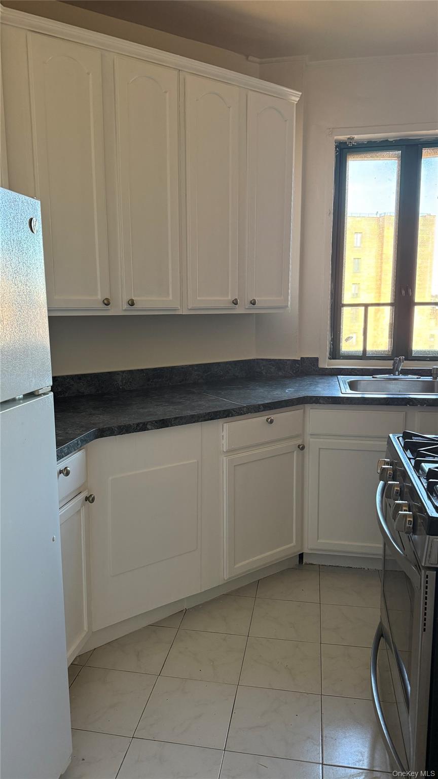 20 Metropolitan Ovl, Unit 11A Bronx, NY 10462 - Photo 5 of 16 Kitchen with white cabinetry, dark countertops, stainless steel gas stove, and freestanding refrigerator
