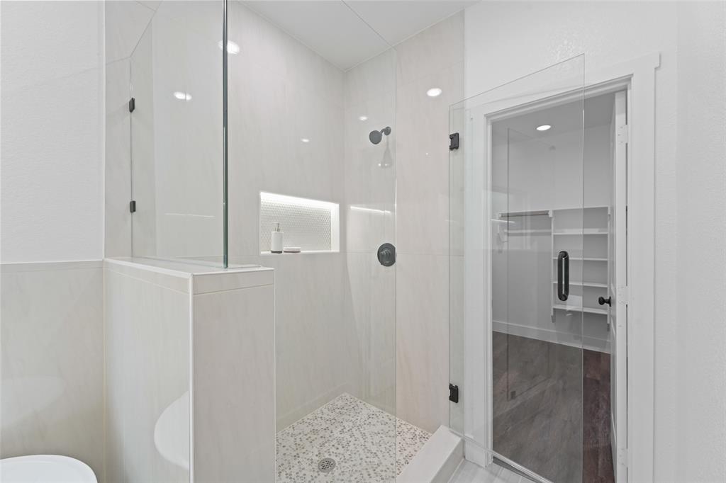 122 East Beachwood Loop Trinidad, TX 75163 - Photo 23 of 35 Walk-in shower featuring a frameless glass enclosure, tiled walls, built-in shelving with accent lighting, dark-finish fixtures, and a pebble-mosaic floor