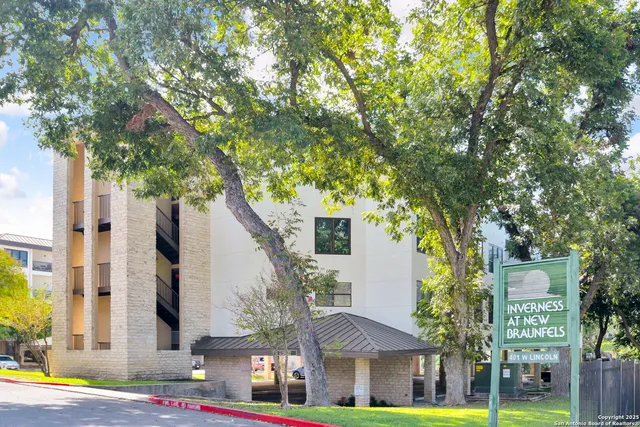 a front view of a building with large trees and plants