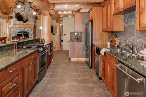 a large kitchen with stainless steel appliances granite countertop a stove a sink dishwasher and a refrigerator with wooden cabinets