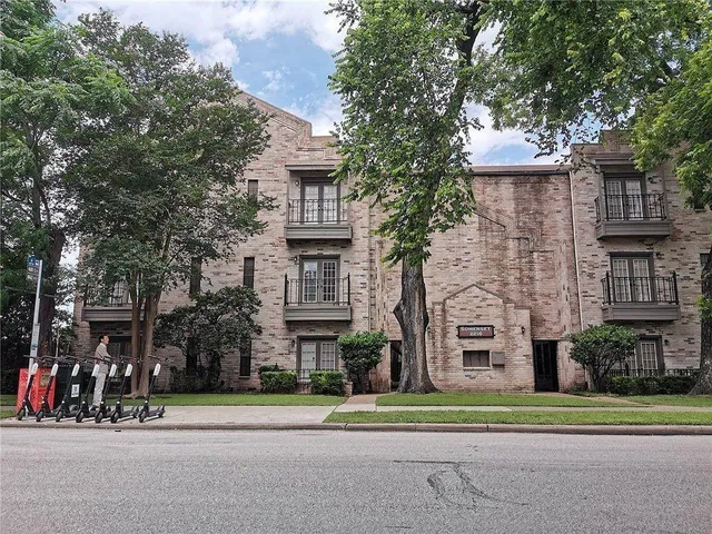 a front view of a building with a garden and trees