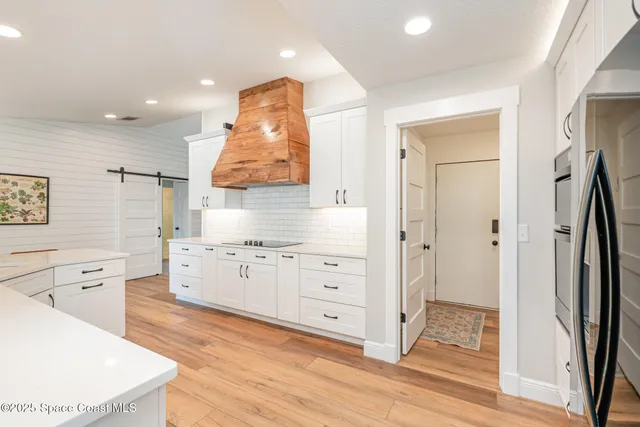 a large white kitchen with a refrigerator a sink dishwasher and white cabinets with wooden floor