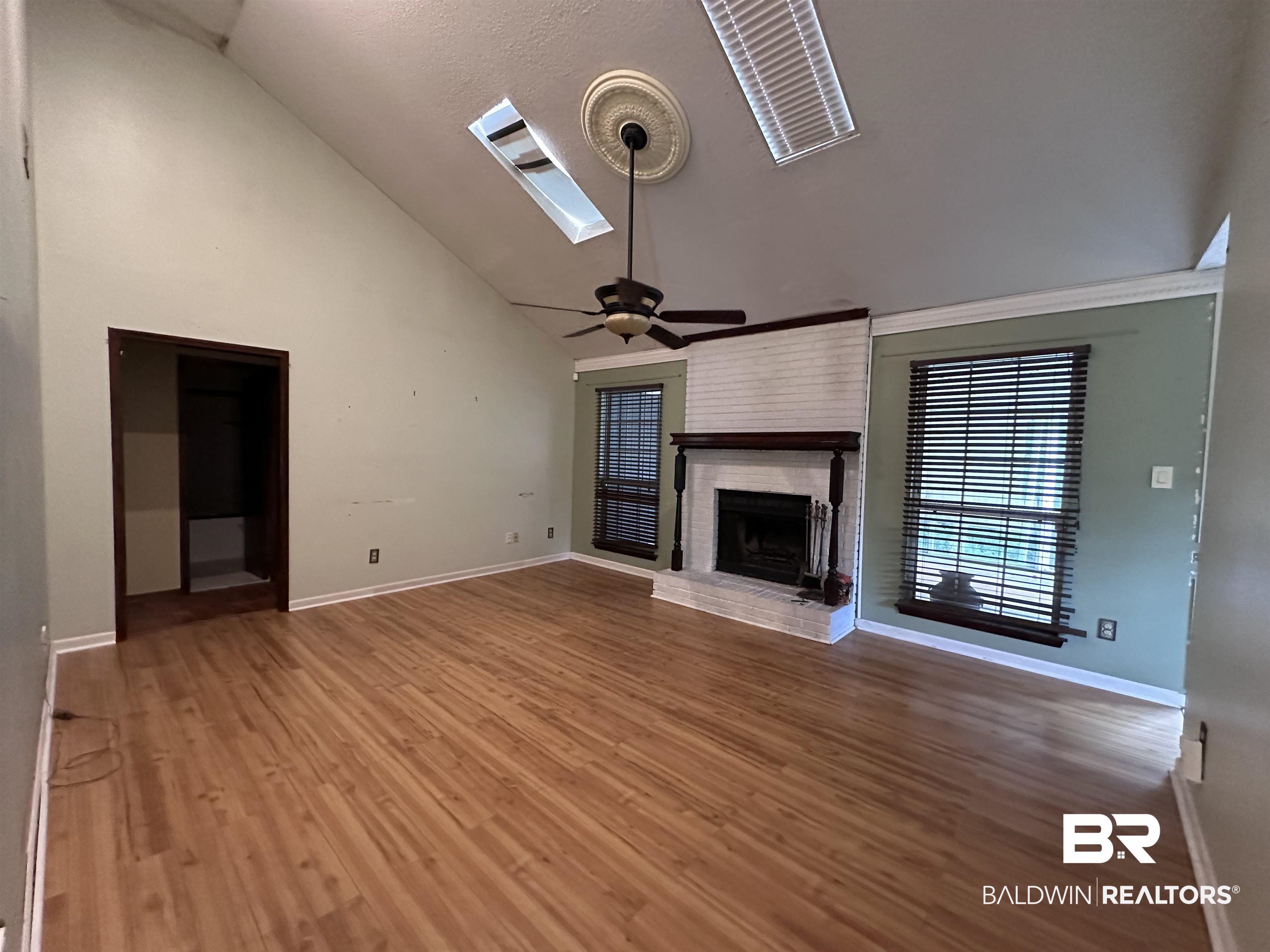 3613 Vista Ridge Drive Mobile, AL 36693 - Photo 3 of 9 Unfurnished living room with a skylight, ceiling fan, a brick fireplace, wood-type flooring, and high vaulted ceiling