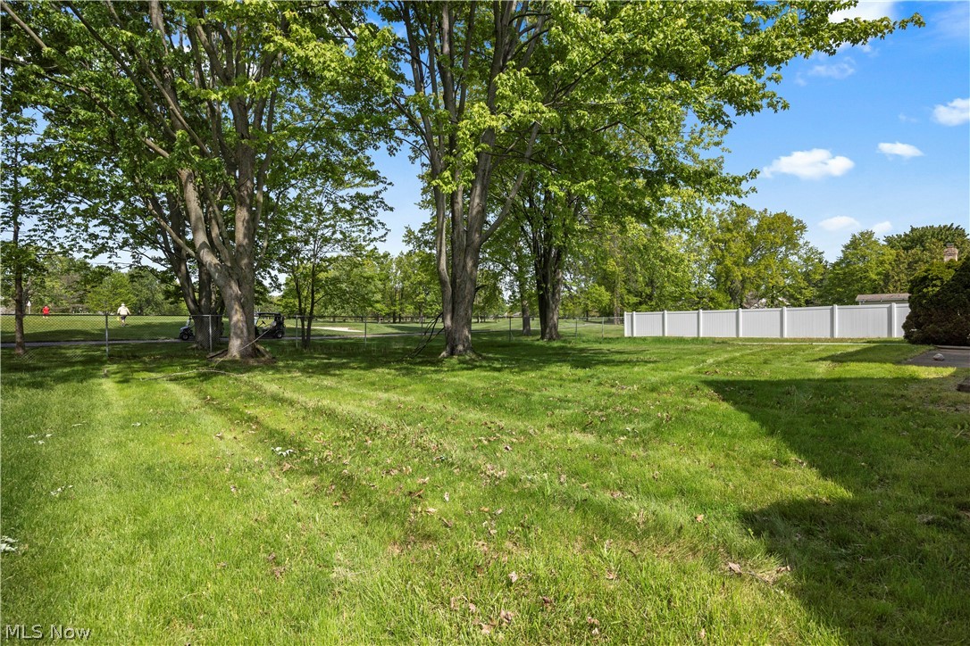722 Jaycox Road Avon Lake, OH 44012 - Photo 47 of 48 Expansive lawn area featuring mature trees, a white privacy fence, and a chain-link fence bordering a distant green space of the golf course