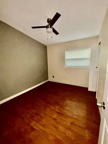 an empty room with wooden floor fan and windows