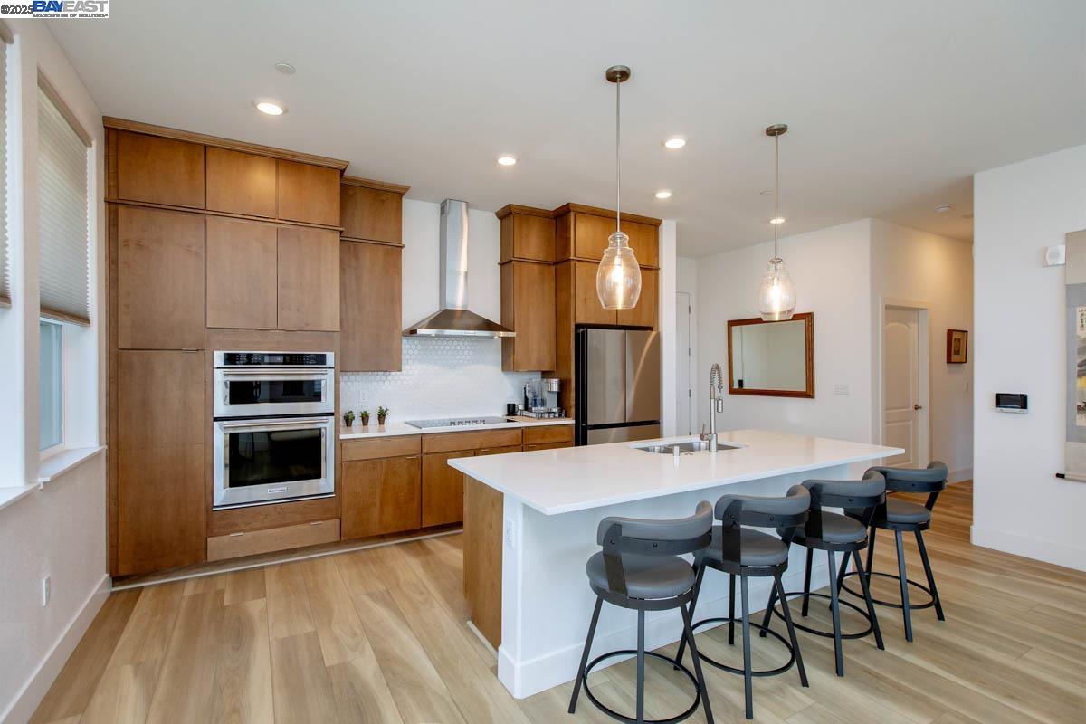 a kitchen with stainless steel appliances a stove a sink a microwave a refrigerator and white cabinets with wooden floor