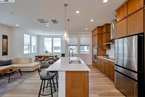 a kitchen with stainless steel appliances granite countertop a refrigerator a sink dishwasher a dining table and chairs with wooden floor