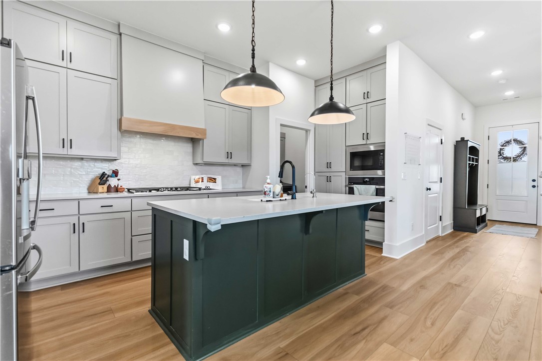 450 Fox Trail Springdale, AR 72762 - Photo 5 of 38 Modern kitchen featuring a dark green island with a light-toned countertop, stainless steel appliances, light gray cabinetry, and wood-finish flooring