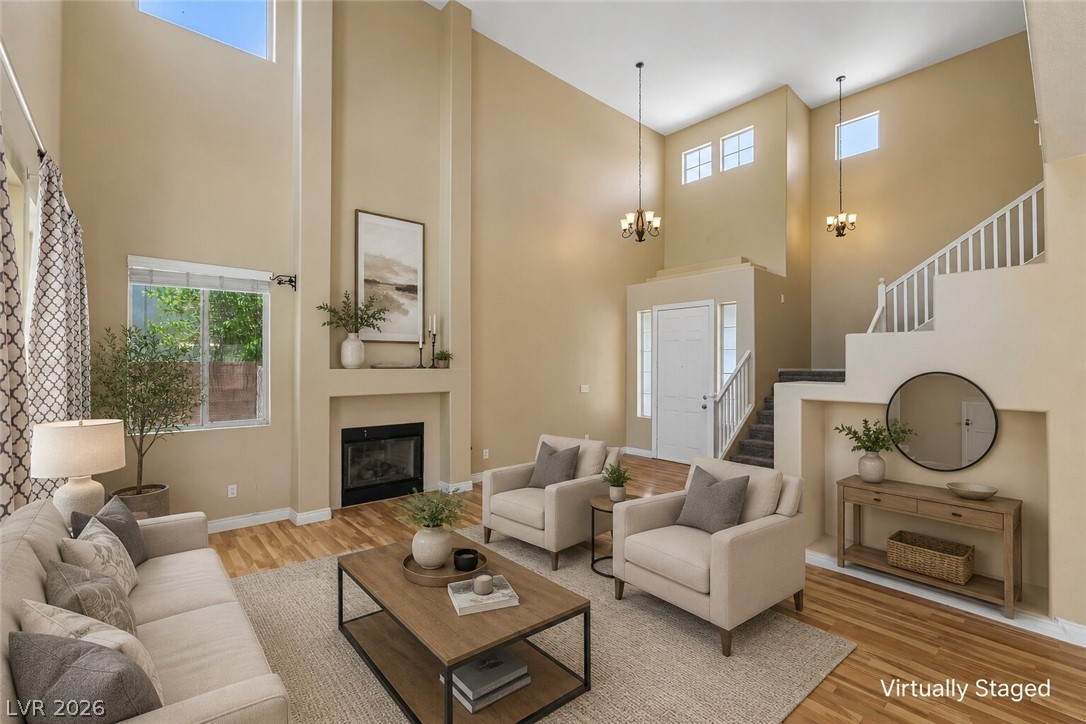 1727 Millstream Way Henderson, NV 89074 - Photo 2 of 46 A spacious living room features soaring ceilings and an elegant fireplace, complemented by natural light and warm hardwood floors.