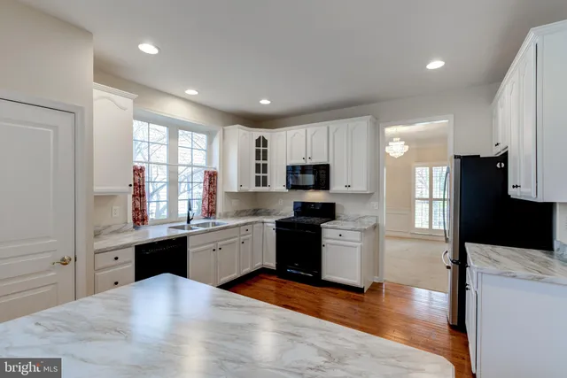 a kitchen with stainless steel appliances granite countertop a refrigerator a sink dishwasher a stove and white cabinets with wooden floor