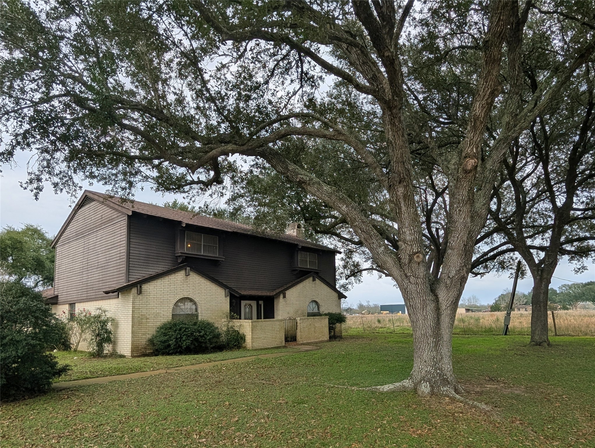 Charming two-story home with a rustic exterior, featuring a mix of brick and hardy board siding. It's set on a spacious lot with mature trees, providing ample shade and a serene atmosphere. Ideal for those seeking a blend of nature and comfort.