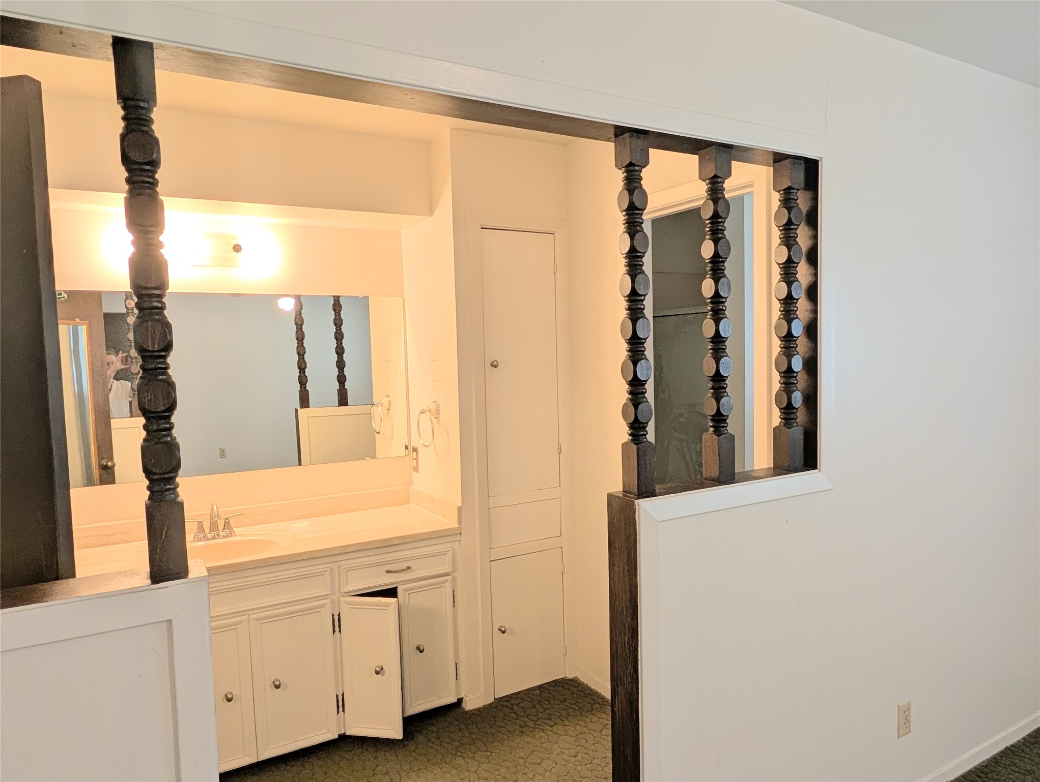 4779 Mixville Road Sealy, TX 77474 - Photo 19 of 47 Vintage-style bathroom with soft white cabinetry, a large mirror, and decorative dark wood spindle accents. The space features a granite countertop sink and has a cozy, retro feel.