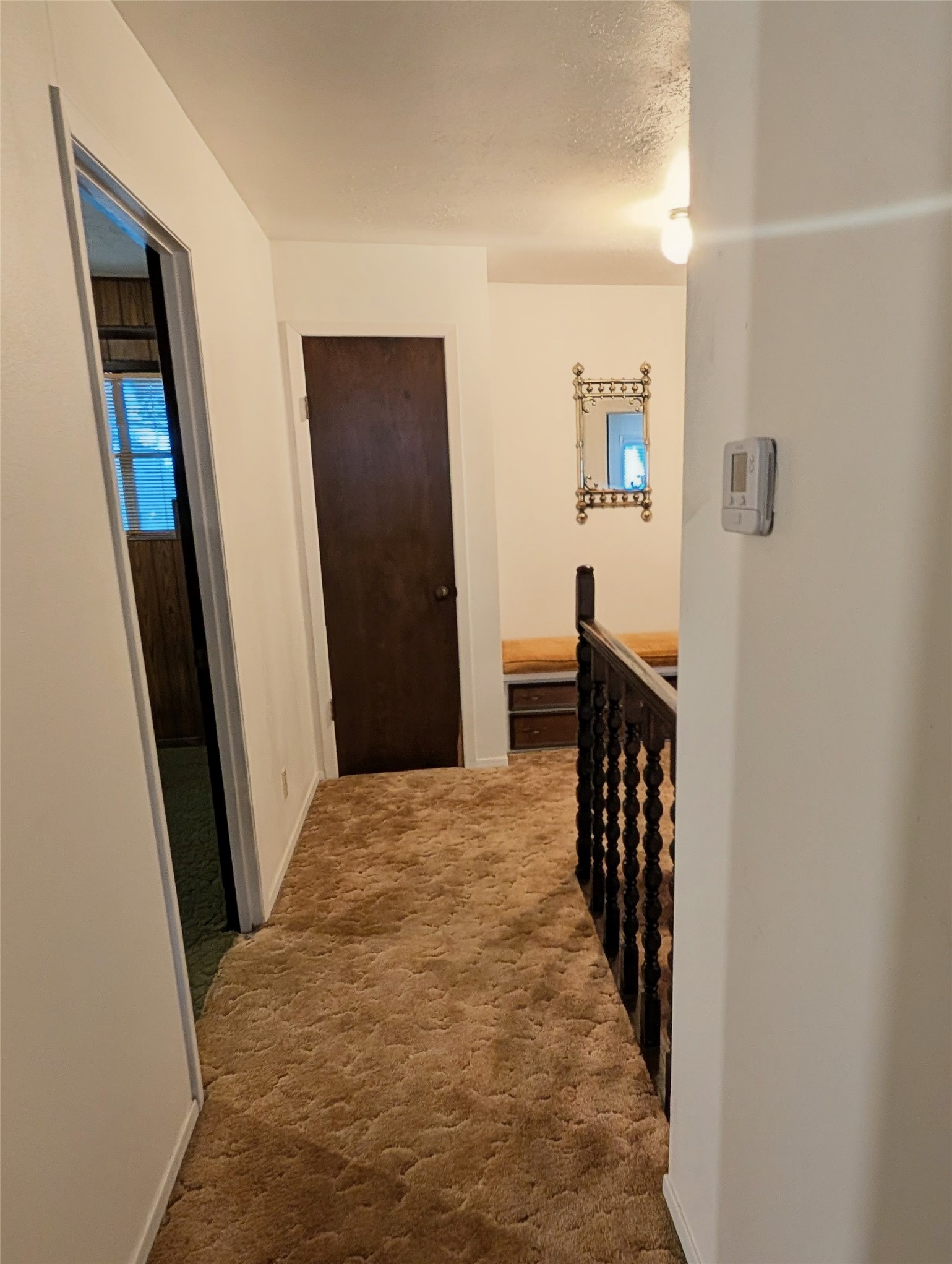 4779 Mixville Road Sealy, TX 77474 - Photo 21 of 47 Upstairs hallway with carpet, white walls, and a dark wooden railing. There’s a closed wooden door and an open doorway leading to another room. A decorative mirror and light fixture add character.