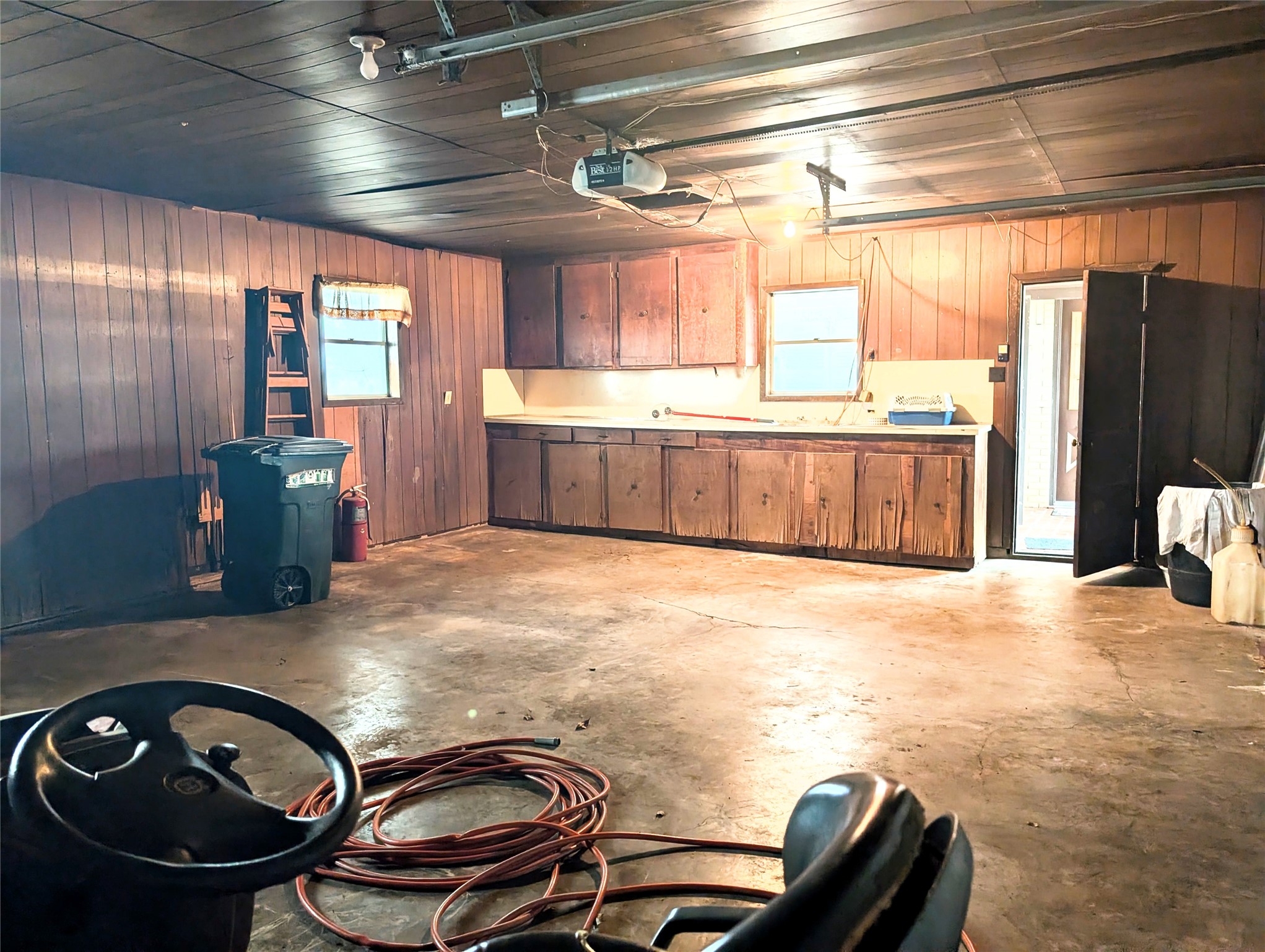 4779 Mixville Road Sealy, TX 77474 - Photo 29 of 47 Spacious garage with wooden paneling, concrete floor, and built-in cabinets. Includes overhead lighting, a garage door opener, and access to an exterior door. Ideal for additional storage or a workshop space.