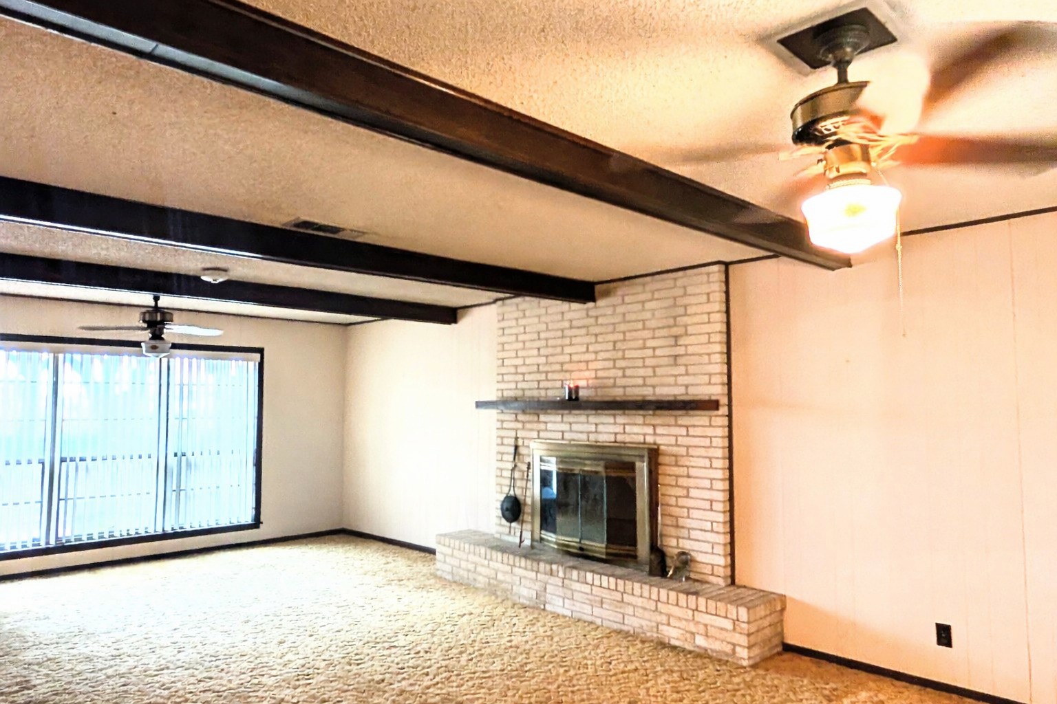 4779 Mixville Road Sealy, TX 77474 - Photo 4 of 47 Spacious living room features a cozy brick fireplace, exposed beams, and ceiling fans. Large windows provide ample natural light and a warm atmosphere.