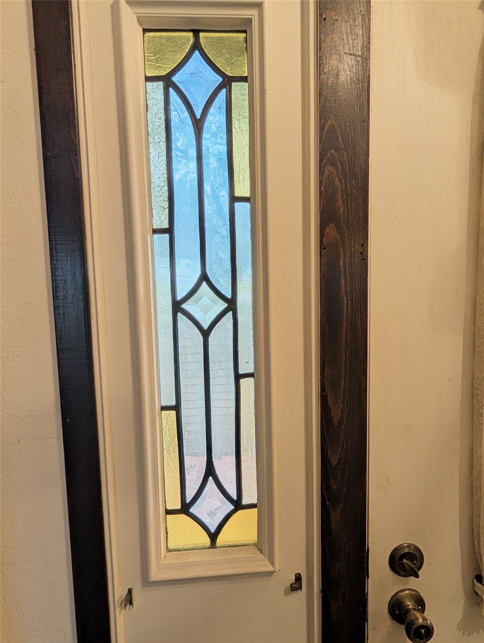 4779 Mixville Road Sealy, TX 77474 - Photo 10 of 47 Close-up of an entrance door panel with a vertical stained glass window featuring a geometric design in yellow, blue, and frosted glass. The door has dark wood trim.