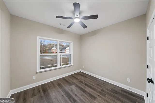 an empty room with wooden floor chandelier fan and windows