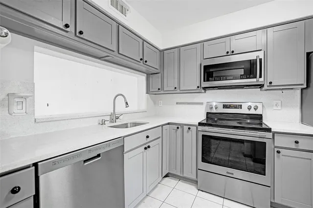 a kitchen with stainless steel appliances granite countertop grey cabinets a stove a sink and dishwasher