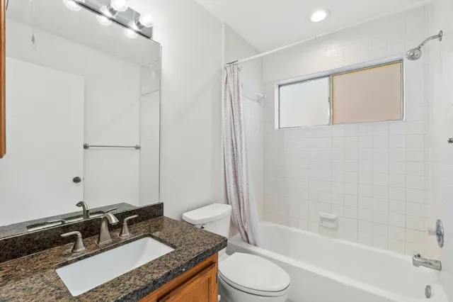 a bathroom with a granite countertop sink a toilet a mirror a bathtub and shower