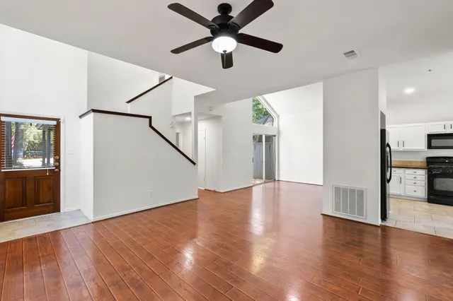 a view of an empty room with wooden floor and a ceiling fan