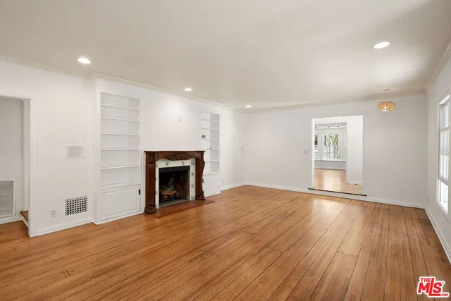 a view of an empty room with wooden floor fireplace and a window