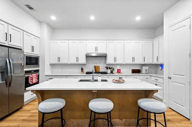 a kitchen with stainless steel appliances granite countertop a sink a stove a refrigerator and white cabinets